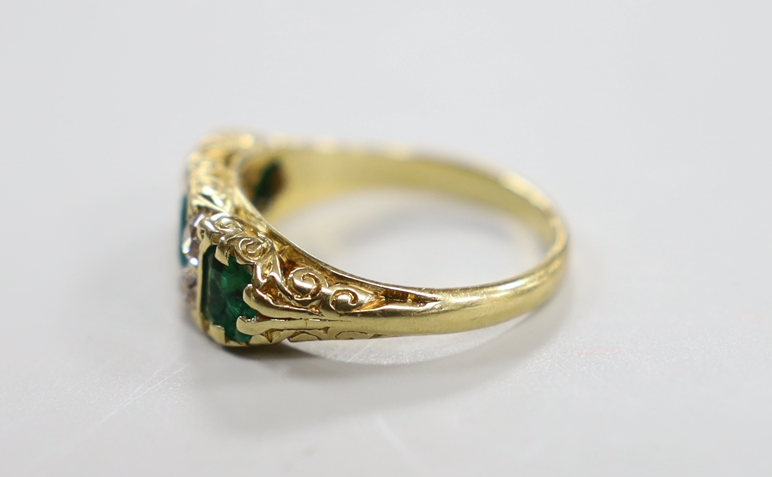 A yellow metal and three stone emerald half hoop ring with four stone diamond set spacers, size M/N, gross weight 4.8 grams.